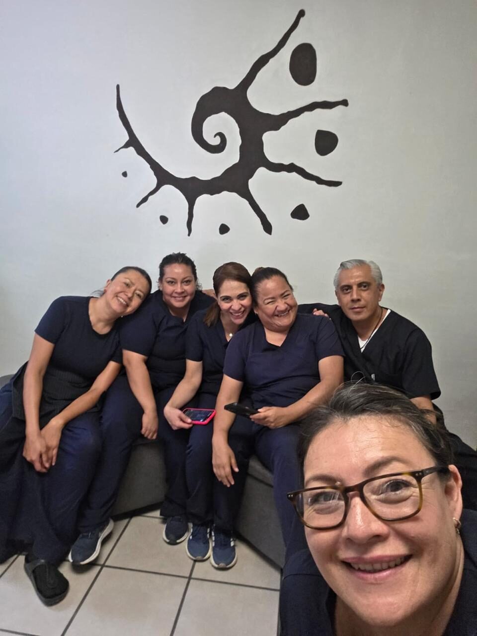 The Paxio team in a selfie, sitting in front of the logo mural
